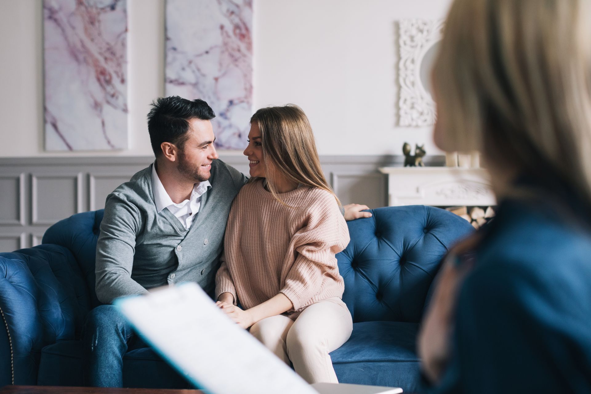 Couple sitting close together on a blue couch in a bright living room, smiling at each other