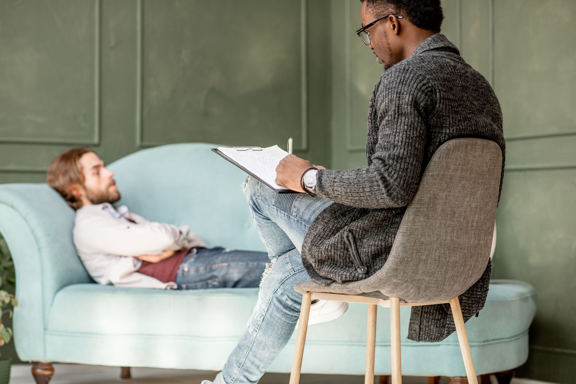 Therapist taking notes while speaking with a client on a couch in a counseling office