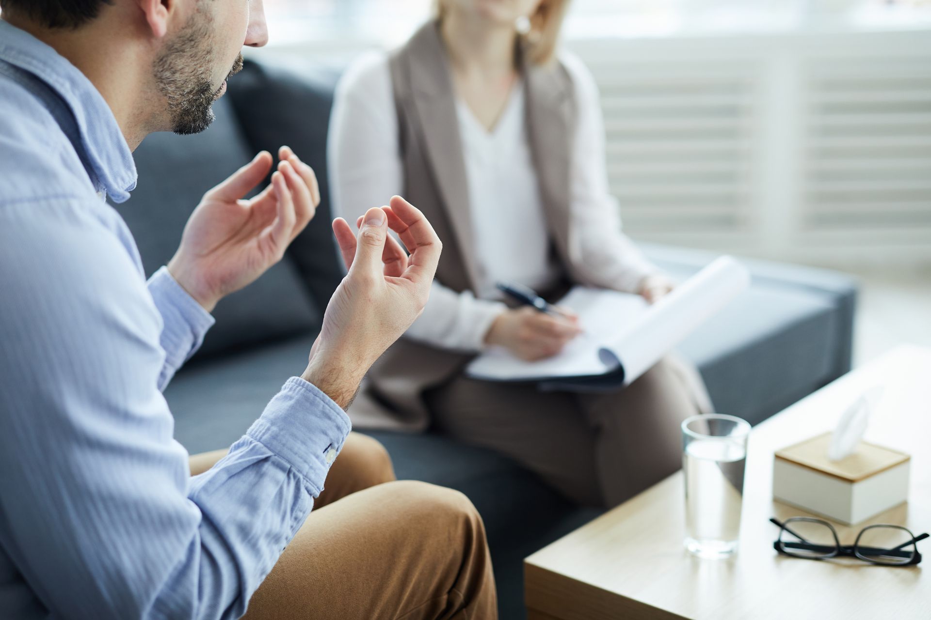 Two people in a meeting, one gesturing while seated across from a notepad and books