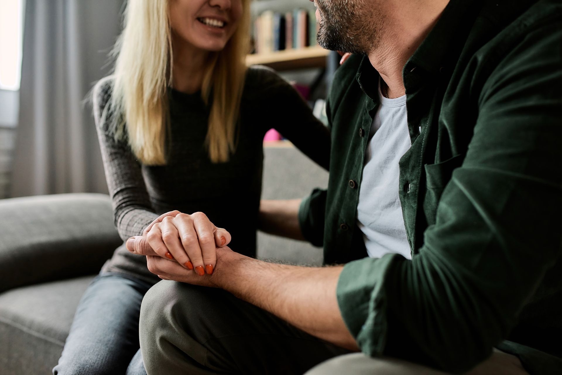 Two people sitting on a couch, holding hands and smiling in a cozy living room