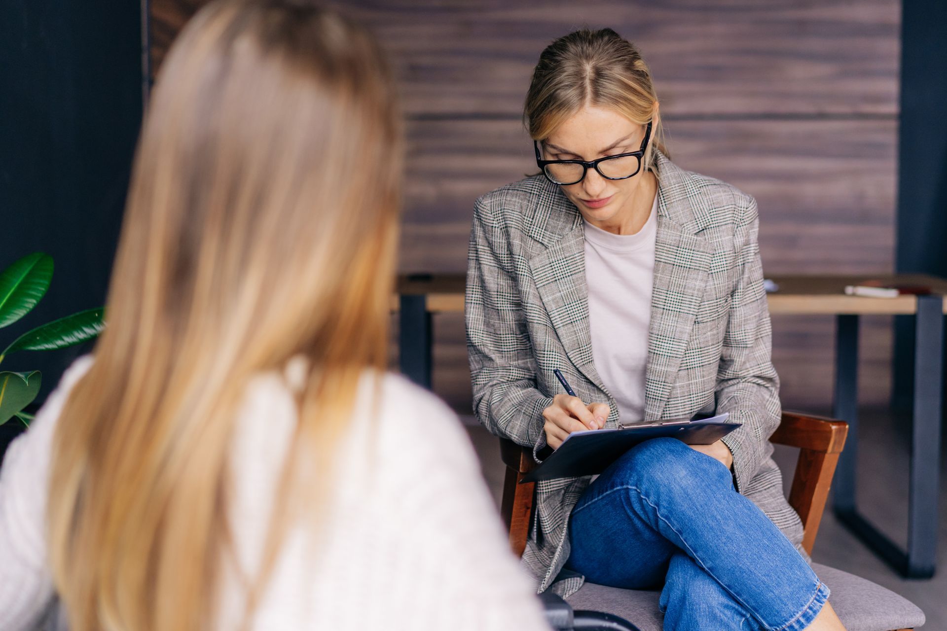 Therapist taking notes during a counseling session with a seated client in a modern office