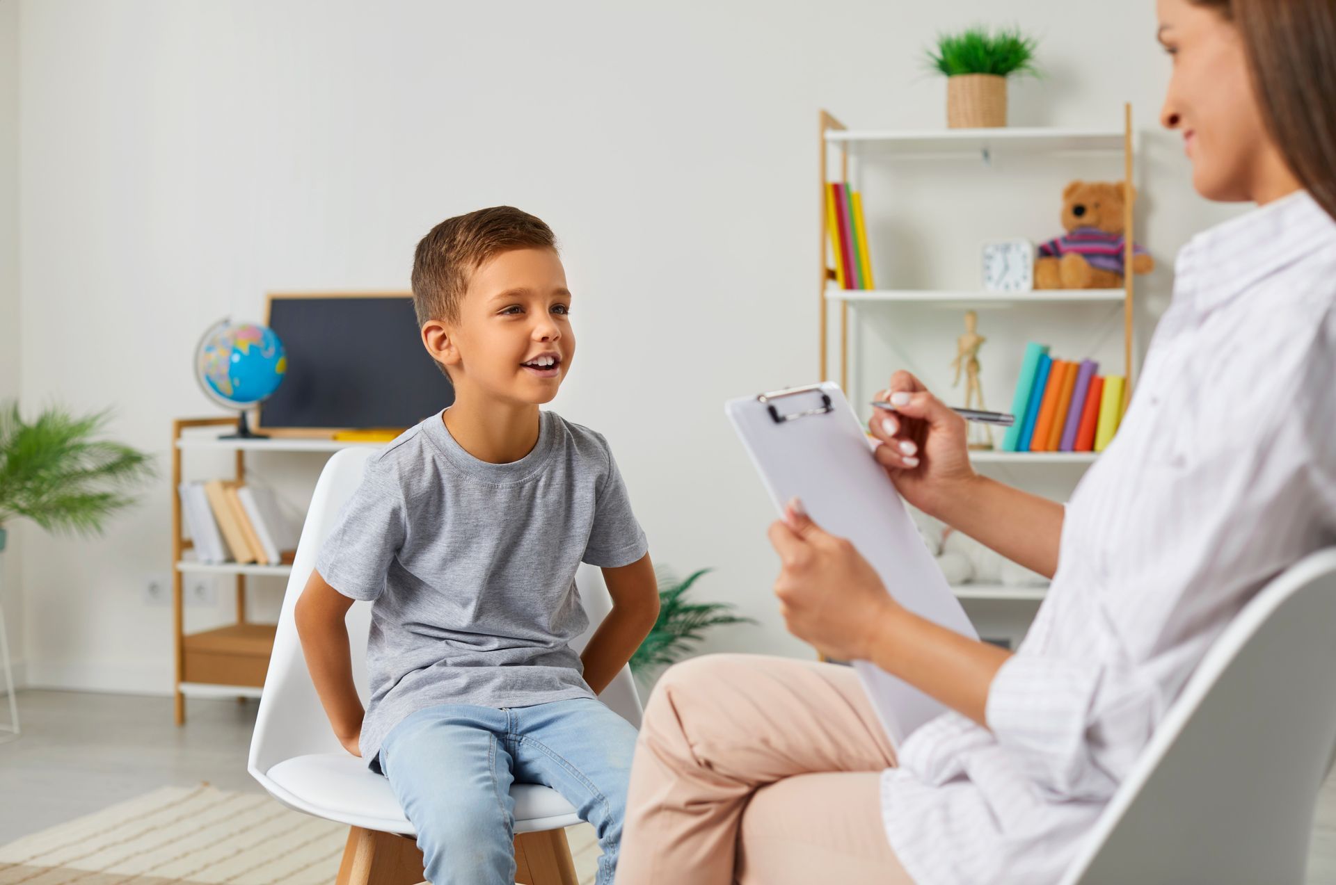 Therapist taking notes while talking with a smiling child in a bright office