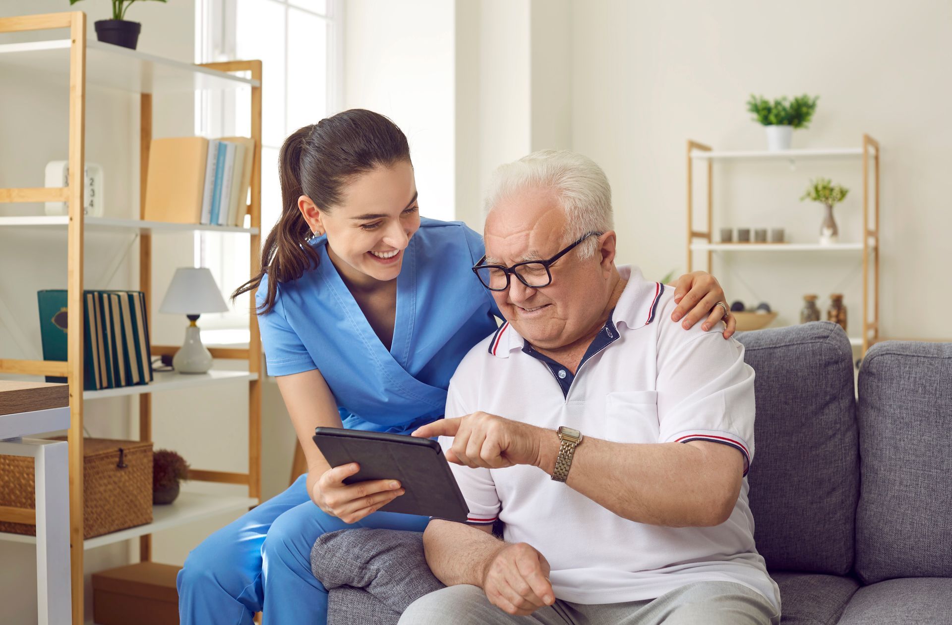 Nurse showing a tablet to an older man on a sofa in a bright living room
