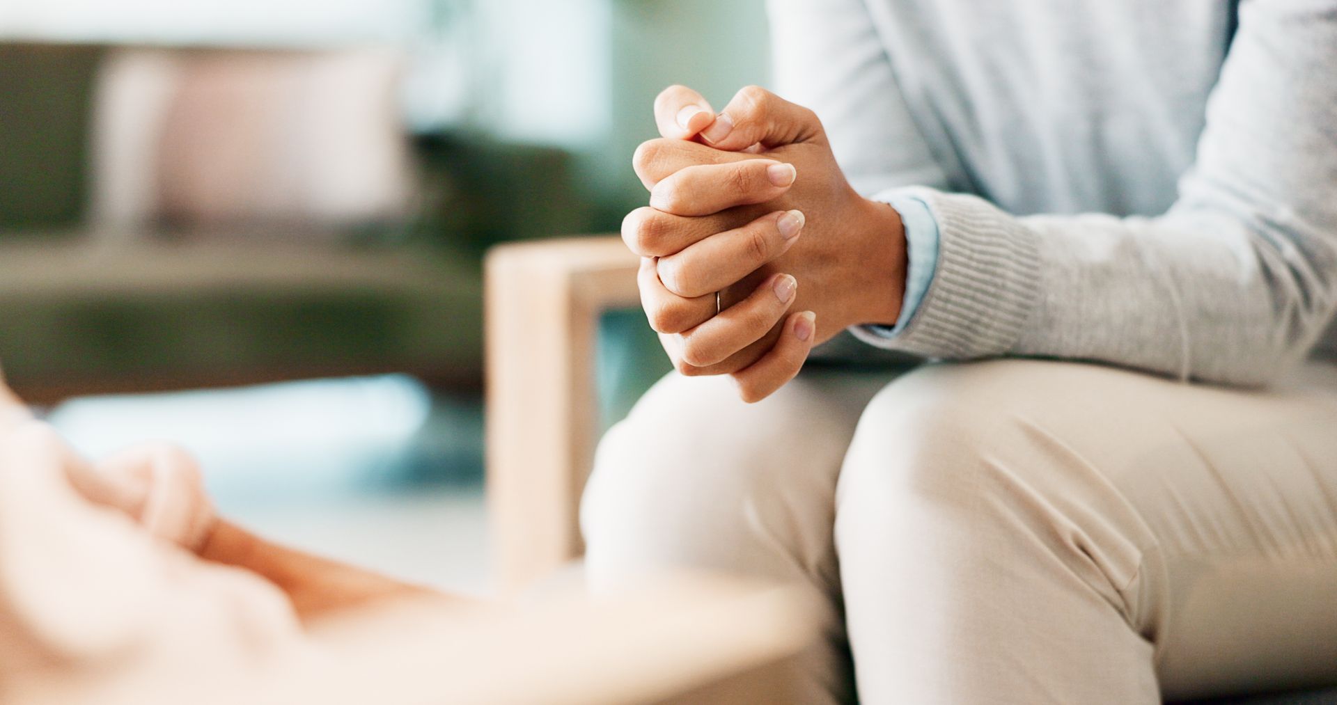 Hands clasped while seated on a sofa in a softly lit room