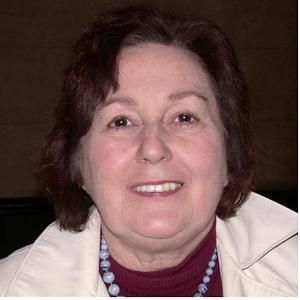 a woman wearing a white jacket and a necklace smiles for the camera .