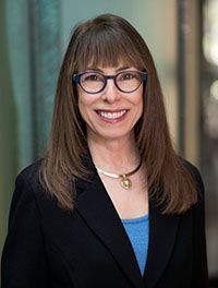 A woman wearing glasses and a black jacket is smiling for the camera.
