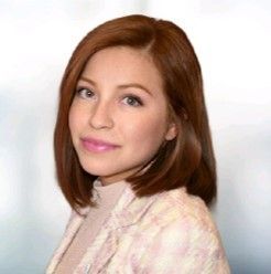 A woman with red hair is wearing a pink jacket and a pink turtleneck.