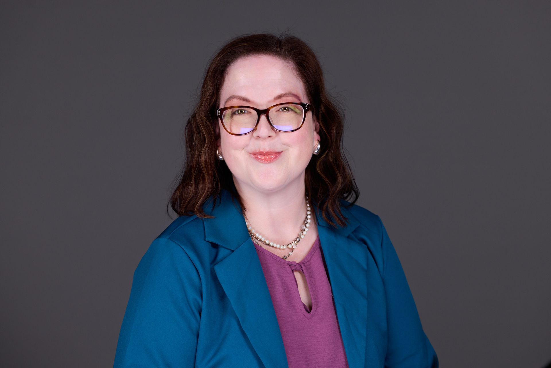 A woman wearing glasses and a necklace is smiling for the camera.