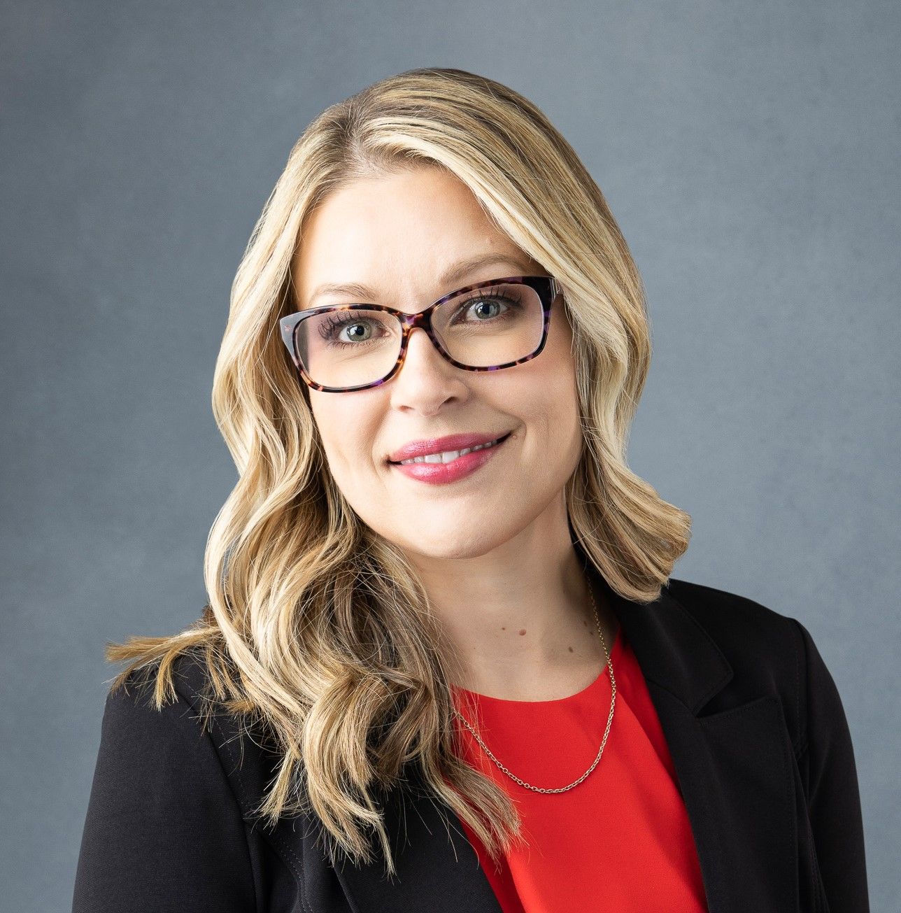 A woman wearing glasses and a red shirt is smiling for the camera.