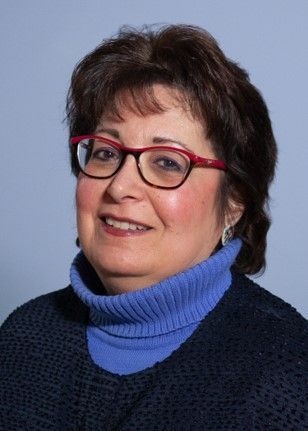 A woman wearing glasses and a blue sweater is smiling for the camera.