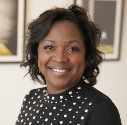 A woman wearing a black shirt with white polka dots is smiling for the camera.