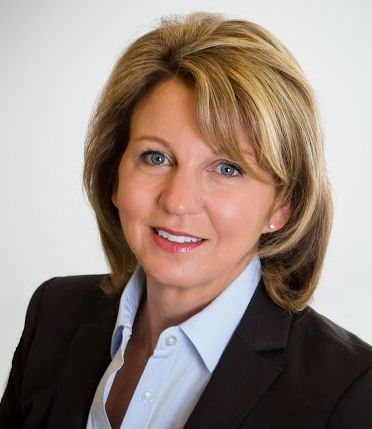 A woman in a suit and blue shirt is smiling for the camera.