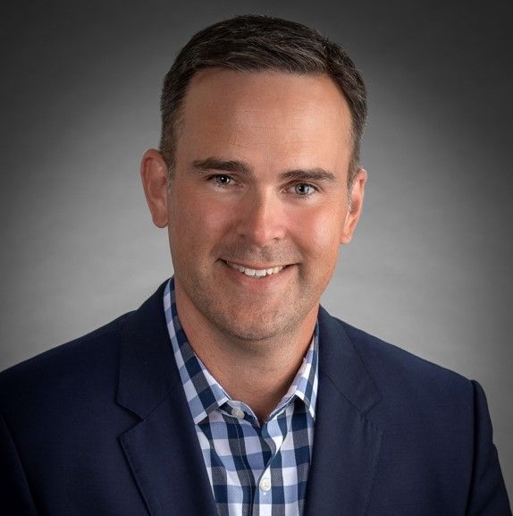 A man in a suit and plaid shirt is smiling for the camera.