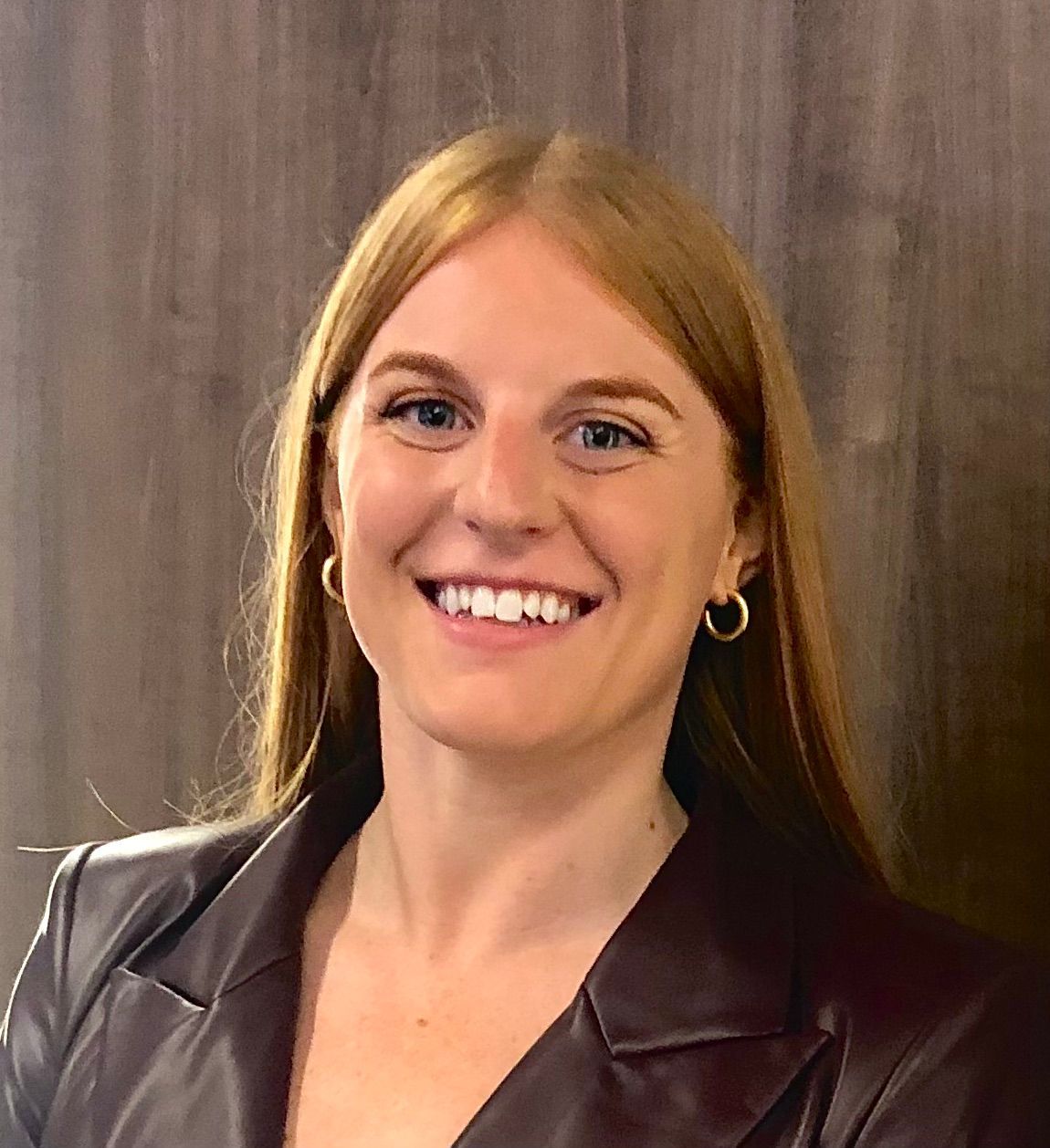 A woman wearing a leather jacket and earrings is smiling for the camera.