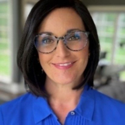 A woman wearing glasses and a blue shirt smiles for the camera