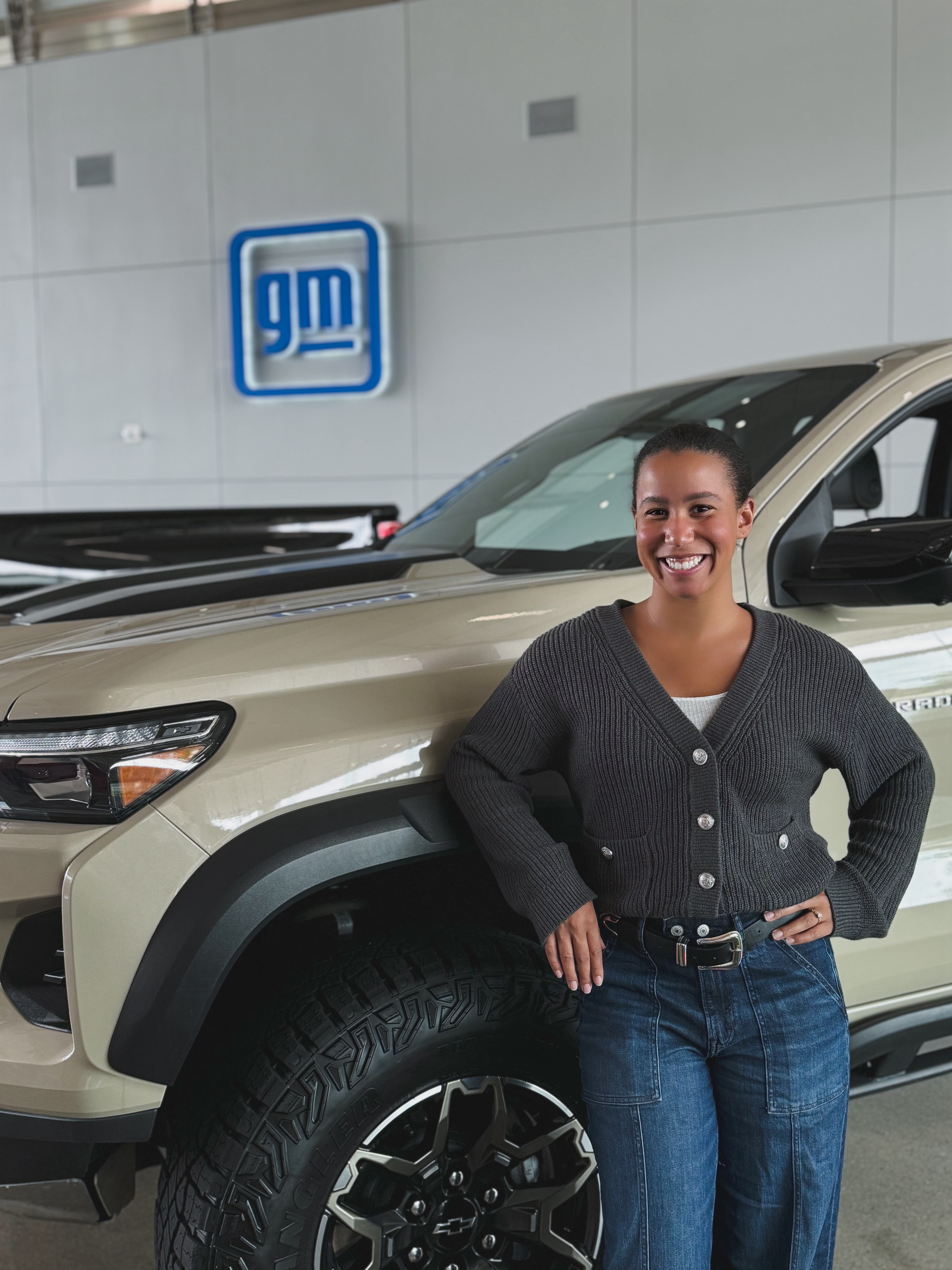A woman is standing next to a gm truck in a showroom.