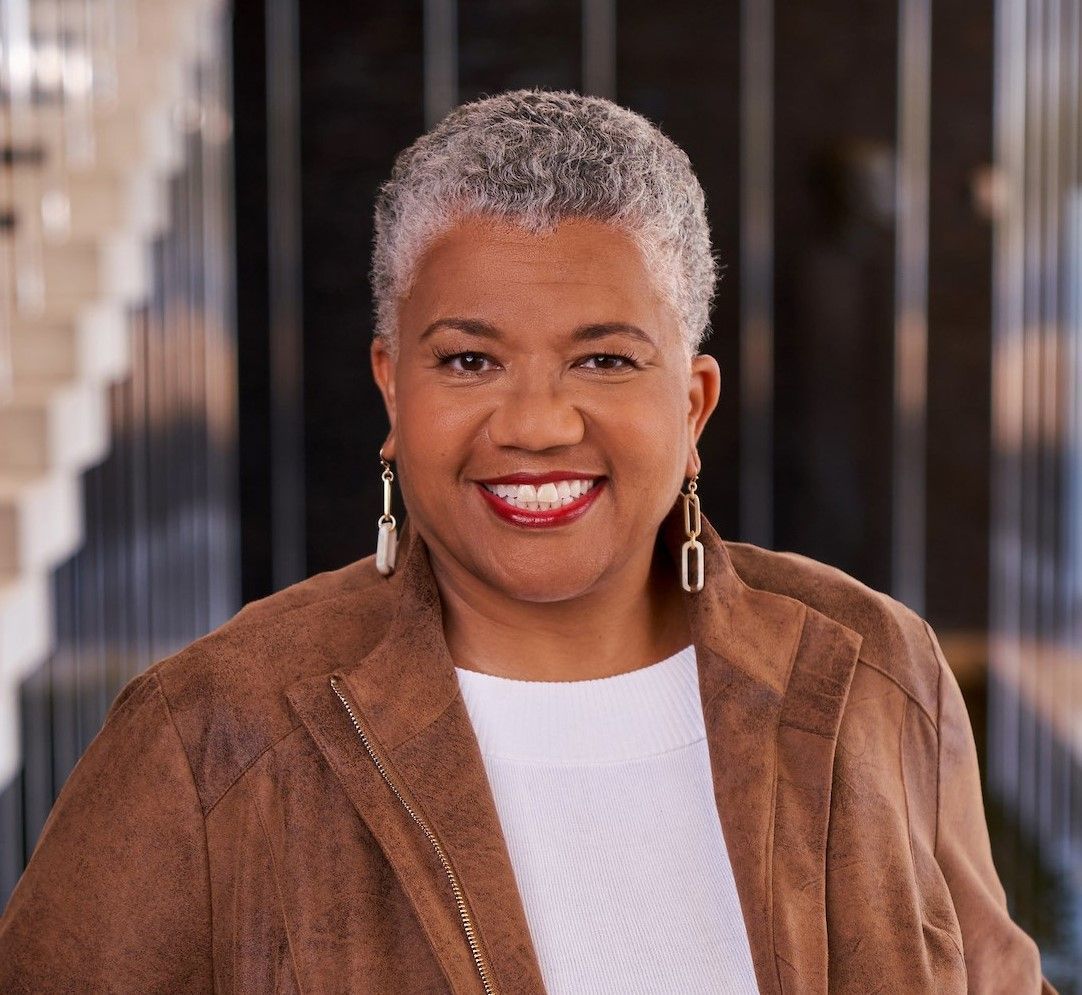 A woman wearing a brown jacket and white shirt is smiling for the camera.