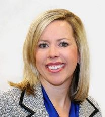 A woman in a suit and blue shirt is smiling for the camera.