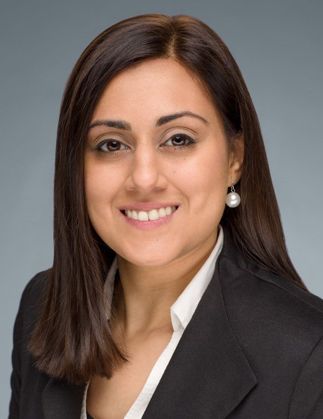 A woman in a suit and pearl earrings is smiling for the camera.