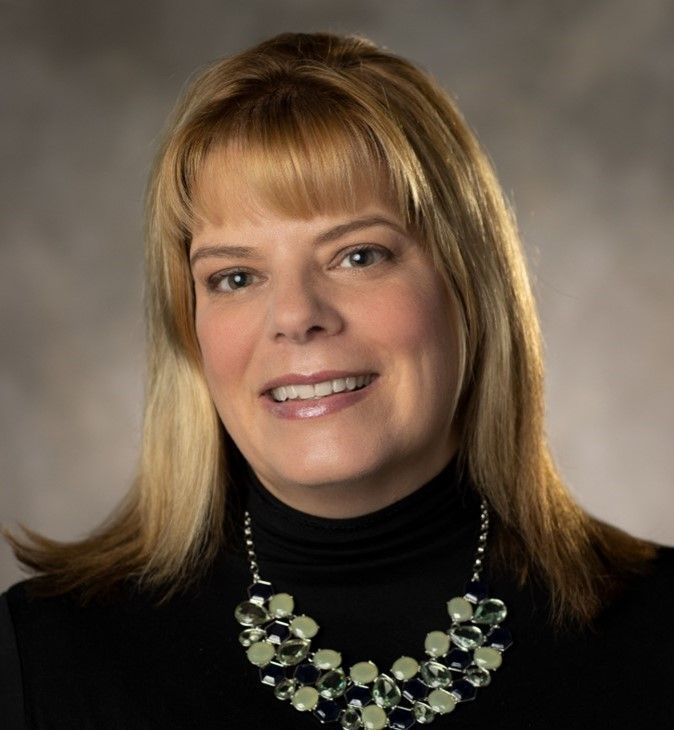 A woman wearing a black turtleneck and a necklace smiles for the camera