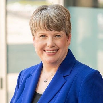 A woman in a blue jacket and necklace is smiling for the camera.