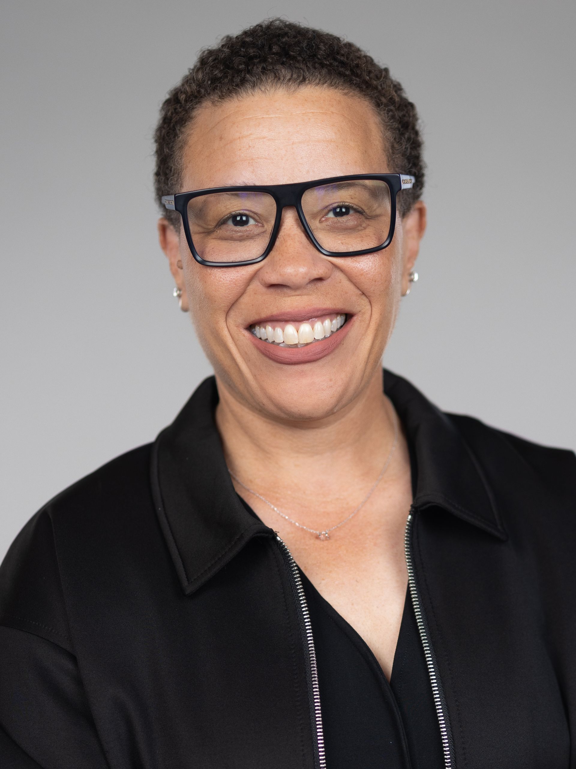 A woman wearing glasses and a blue shirt is smiling for the camera.
