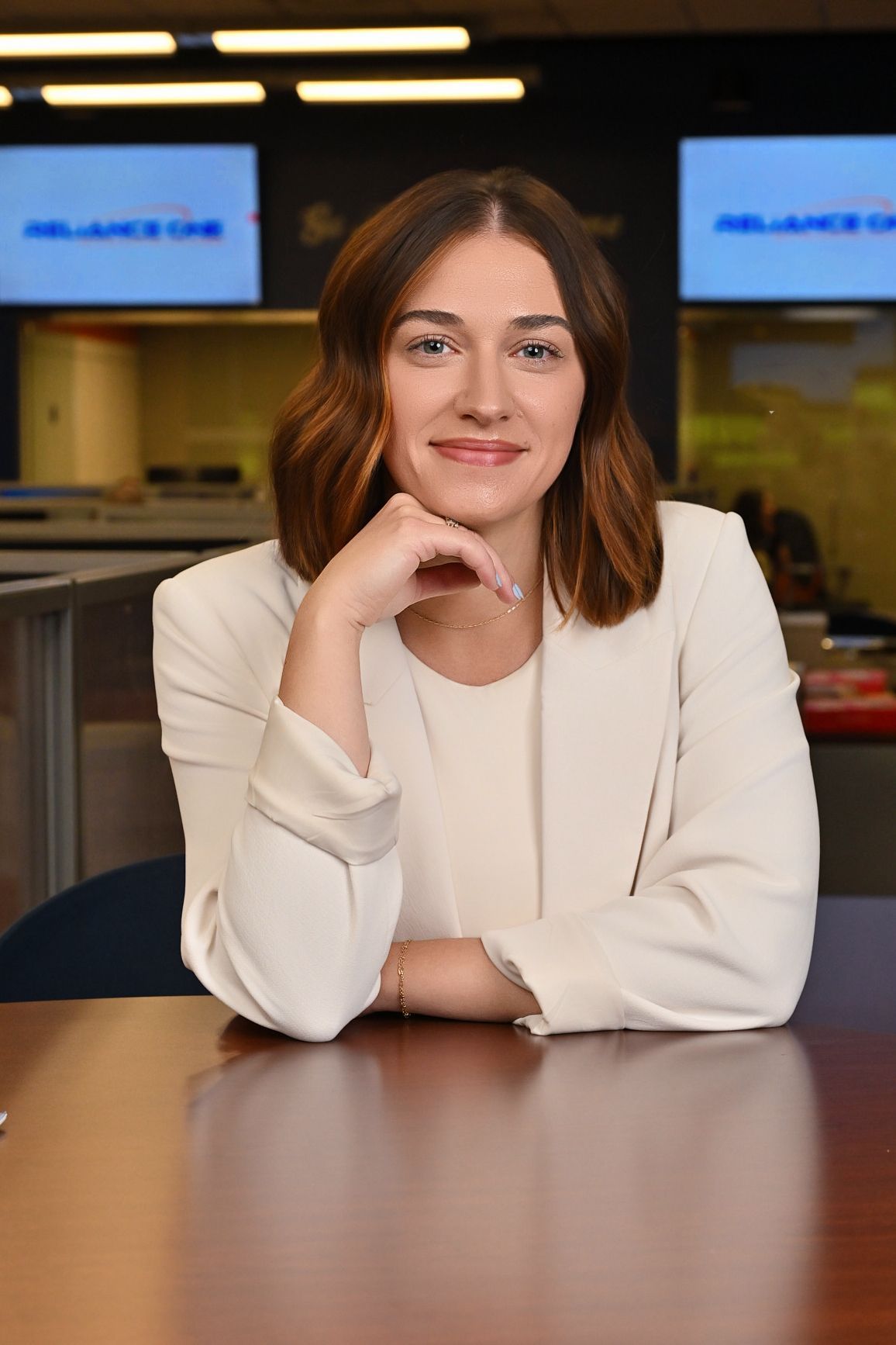 A woman with long brown hair is smiling and wearing a black jacket.