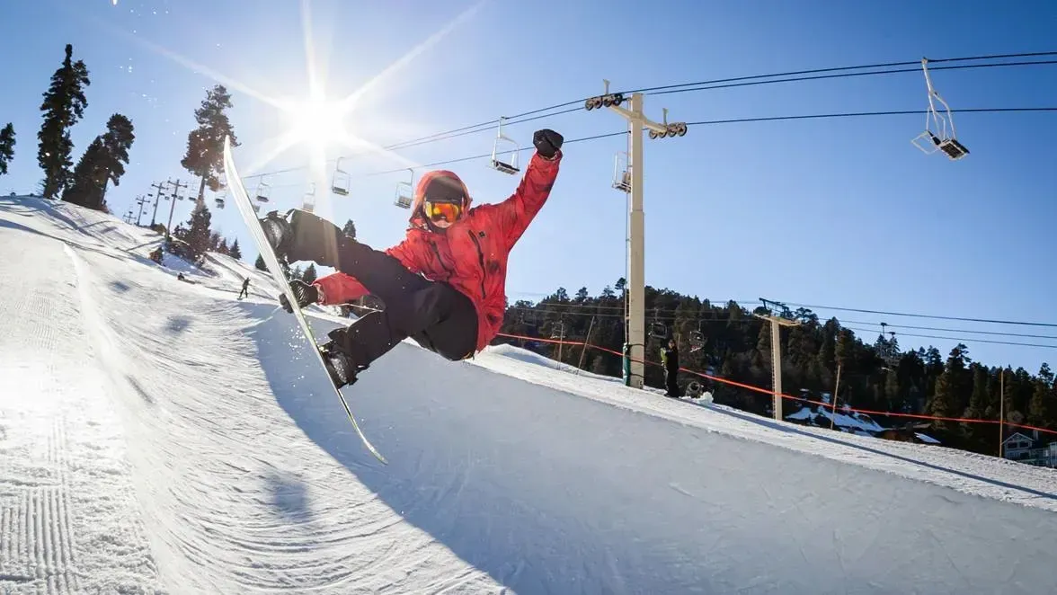 Skier in a red jacket catching air over a snowy slope on a sunny day