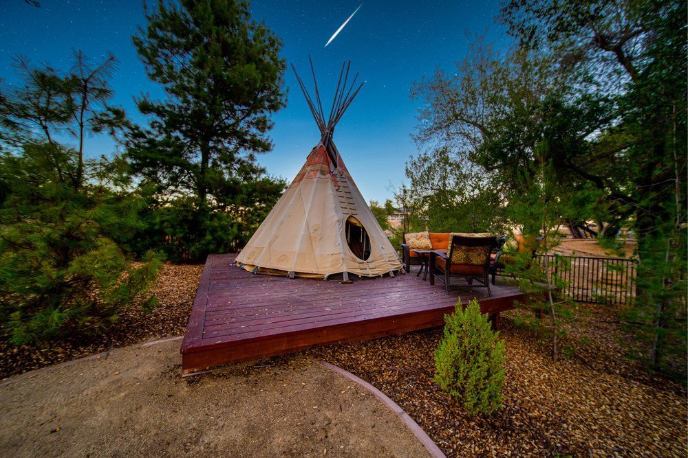a teepee is sitting on top of a wooden deck in the middle of a forest.