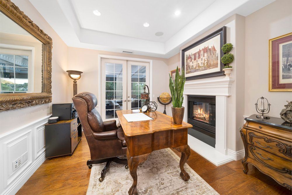 a home office with a desk, chair, fireplace and mirror.