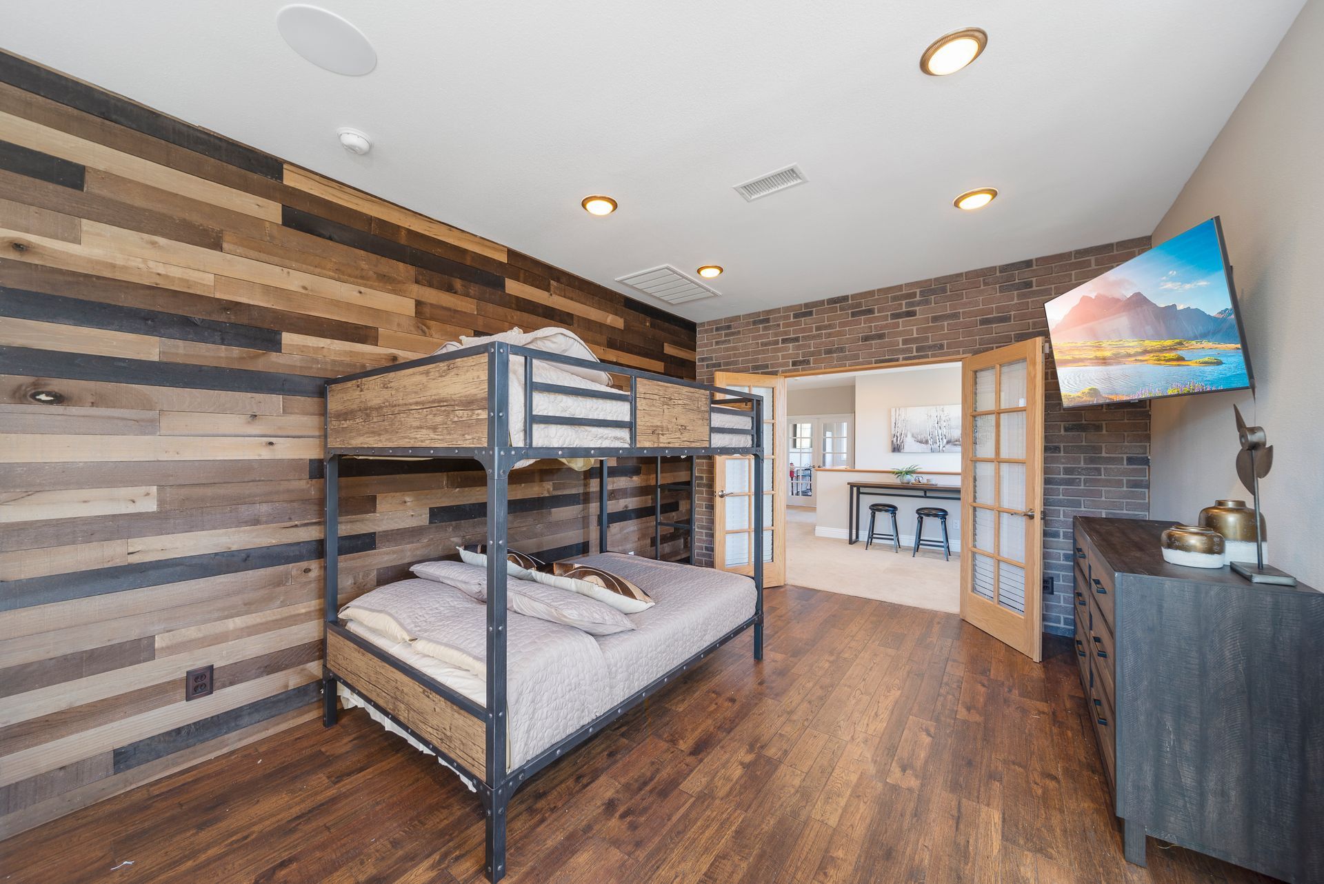 Modern bedroom with black metal bunk bed, wood walls, hardwood floor, and a TV on a dresser