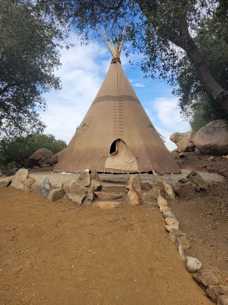 a teepee is sitting on top of a dirt hill surrounded by rocks and trees
