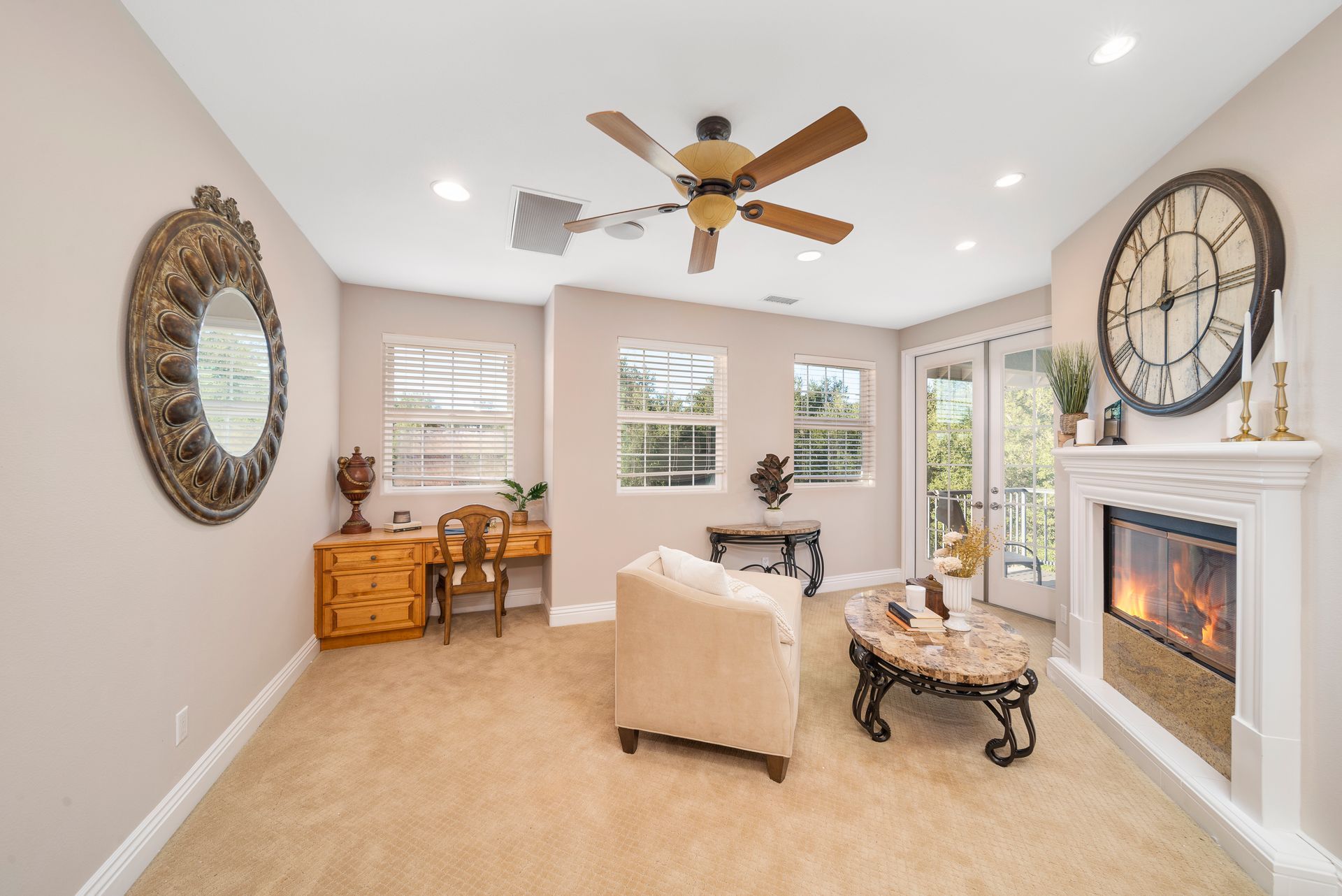Bright living room with fireplace, beige carpet, ceiling fan, and mirrored wall decor