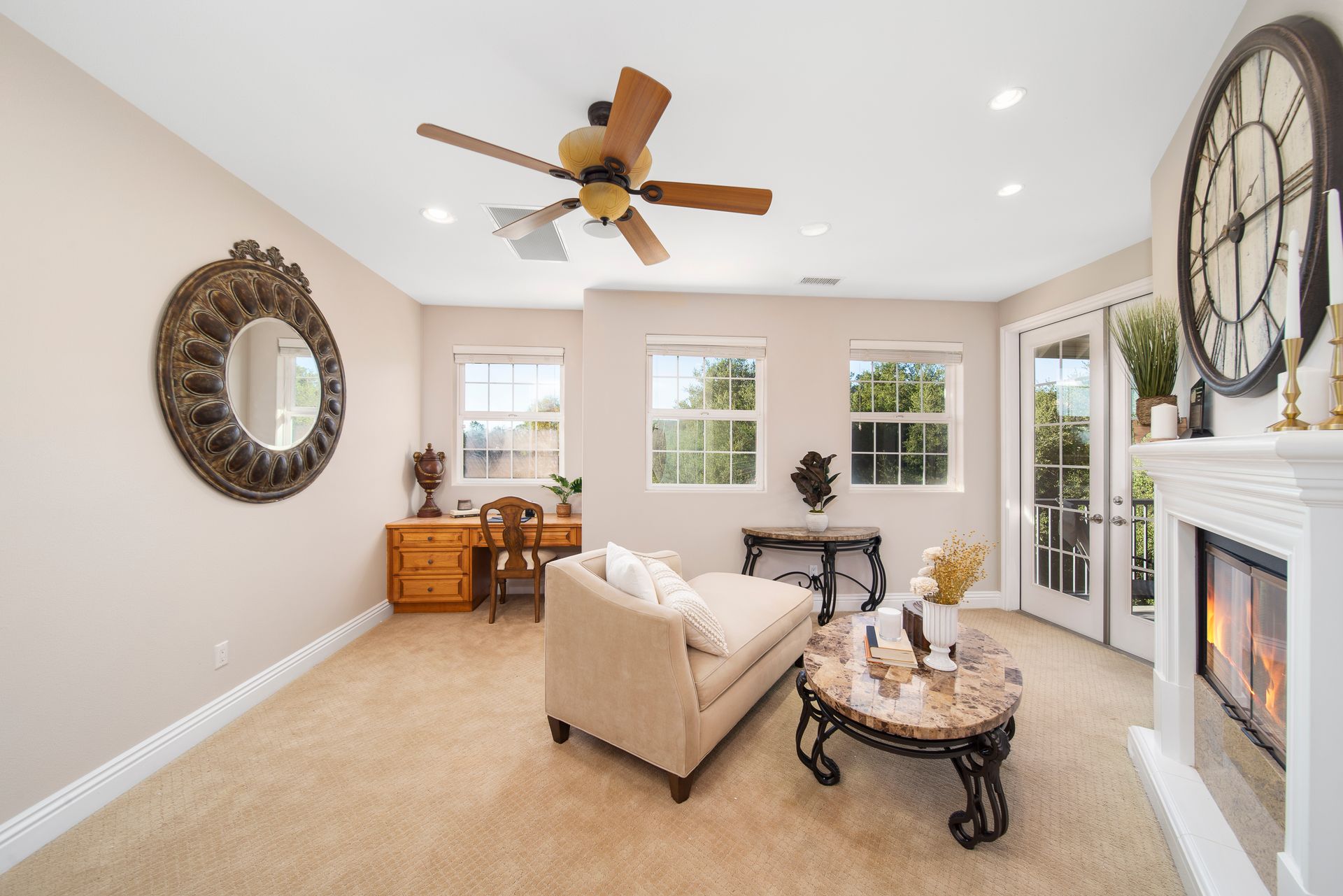 Bright living room with beige sofa, fireplace, large clock, desk, and ceiling fan