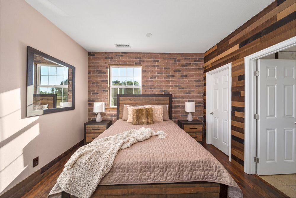 a bedroom with a bed, two nightstands, a mirror and a brick wall