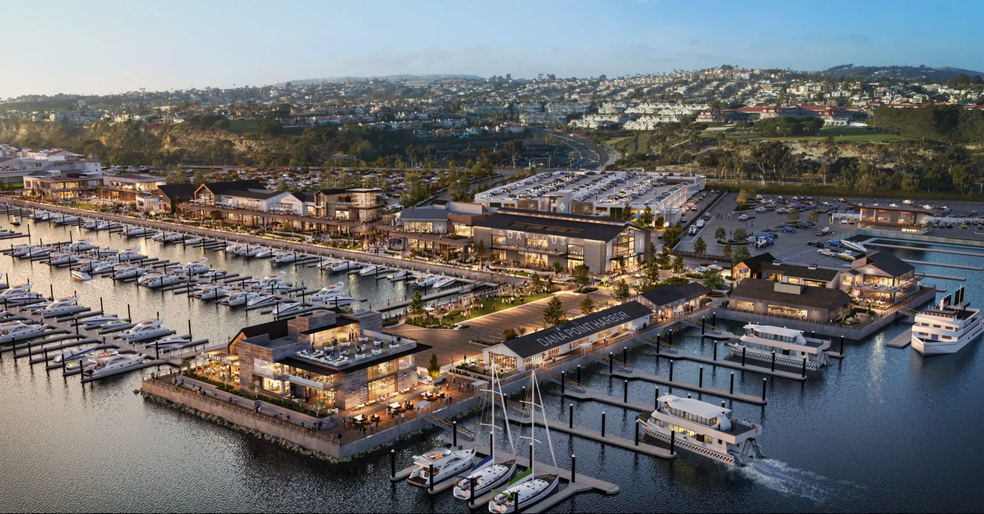 Aerial view of a luxury marina with yachts, docks, and waterfront buildings at sunset.