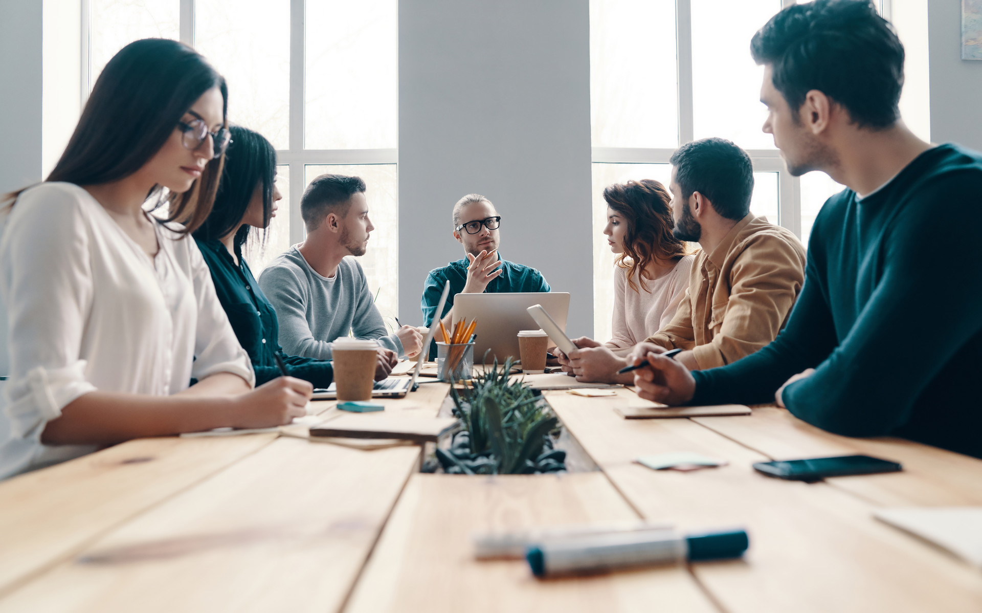 a group of people are sitting around a wooden table having a meeting .
