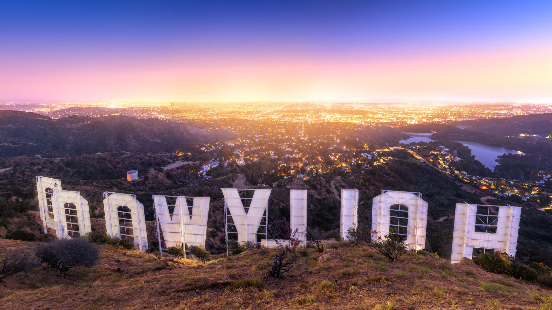 the hollywood sign is sitting on top of a hill overlooking a city at sunset .