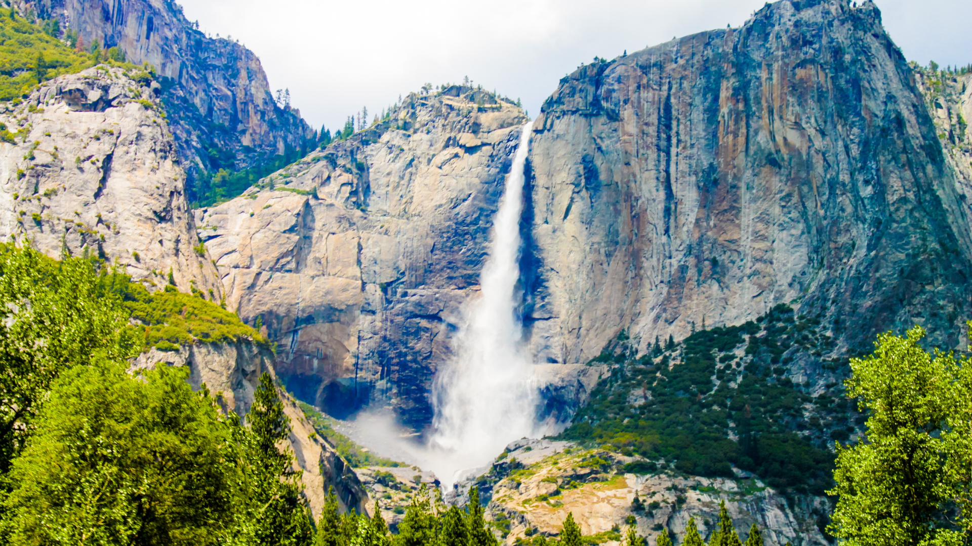 a waterfall in the middle of a mountain surrounded by trees
