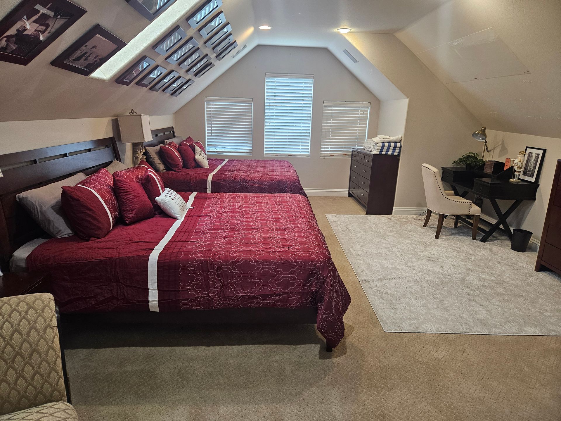 Cozy attic bedroom with two red beds, beige carpet, skylight, and small desk by the window.