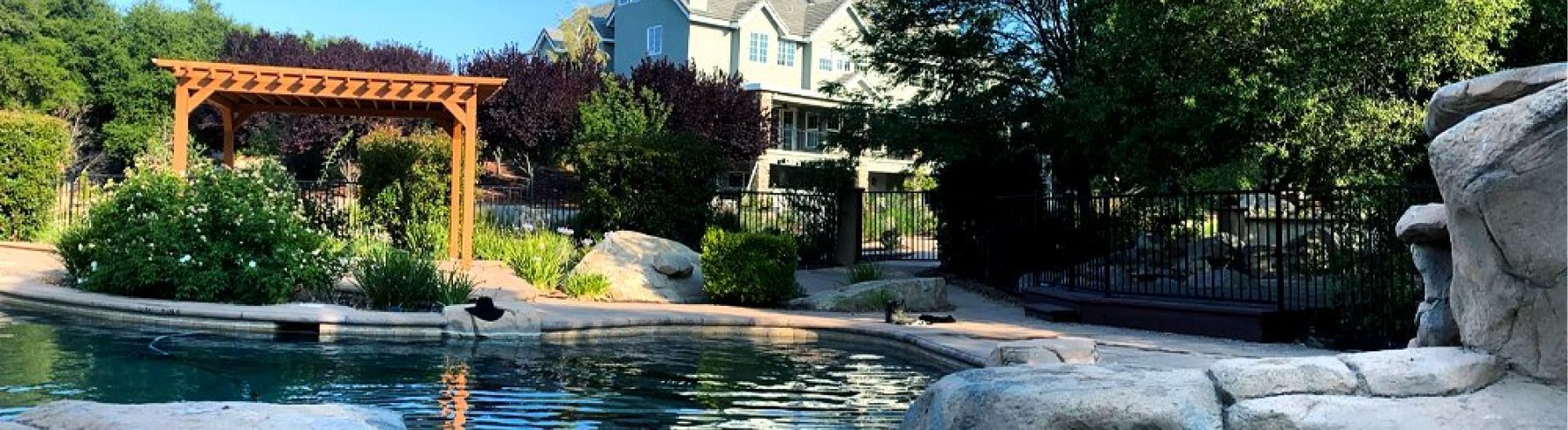 a large swimming pool surrounded by trees and a pergola in a backyard