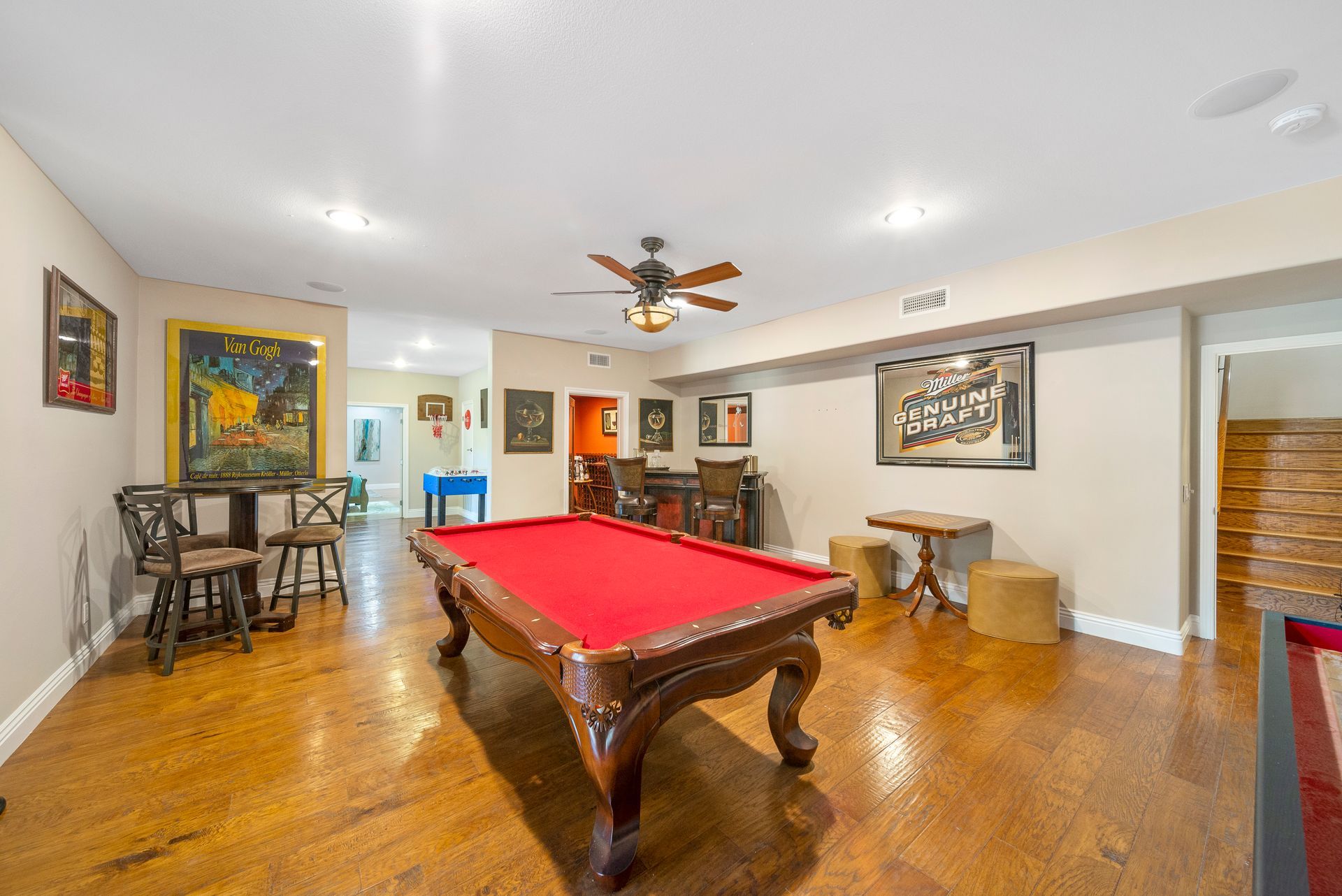 Game room with red pool table, hardwood floors, ceiling fan, and framed artwork on white walls