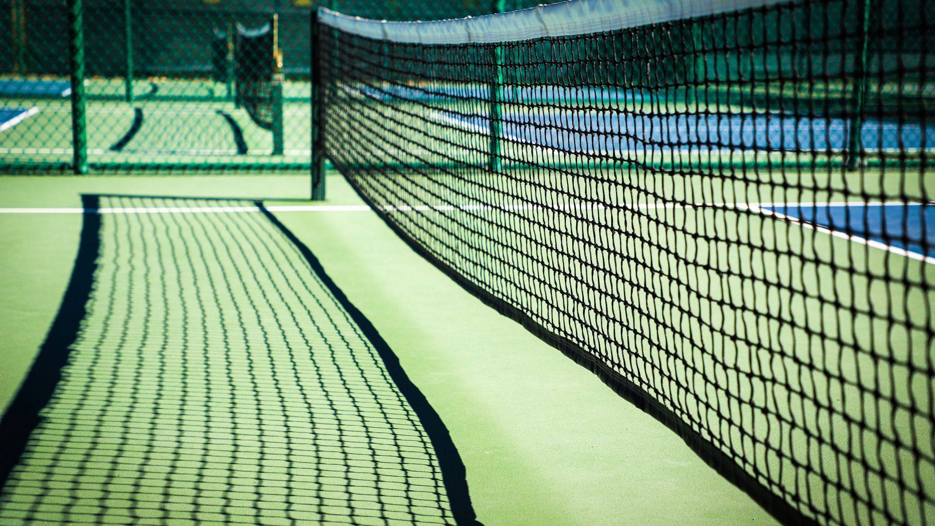 A tennis net on a tennis court with a person in the background
