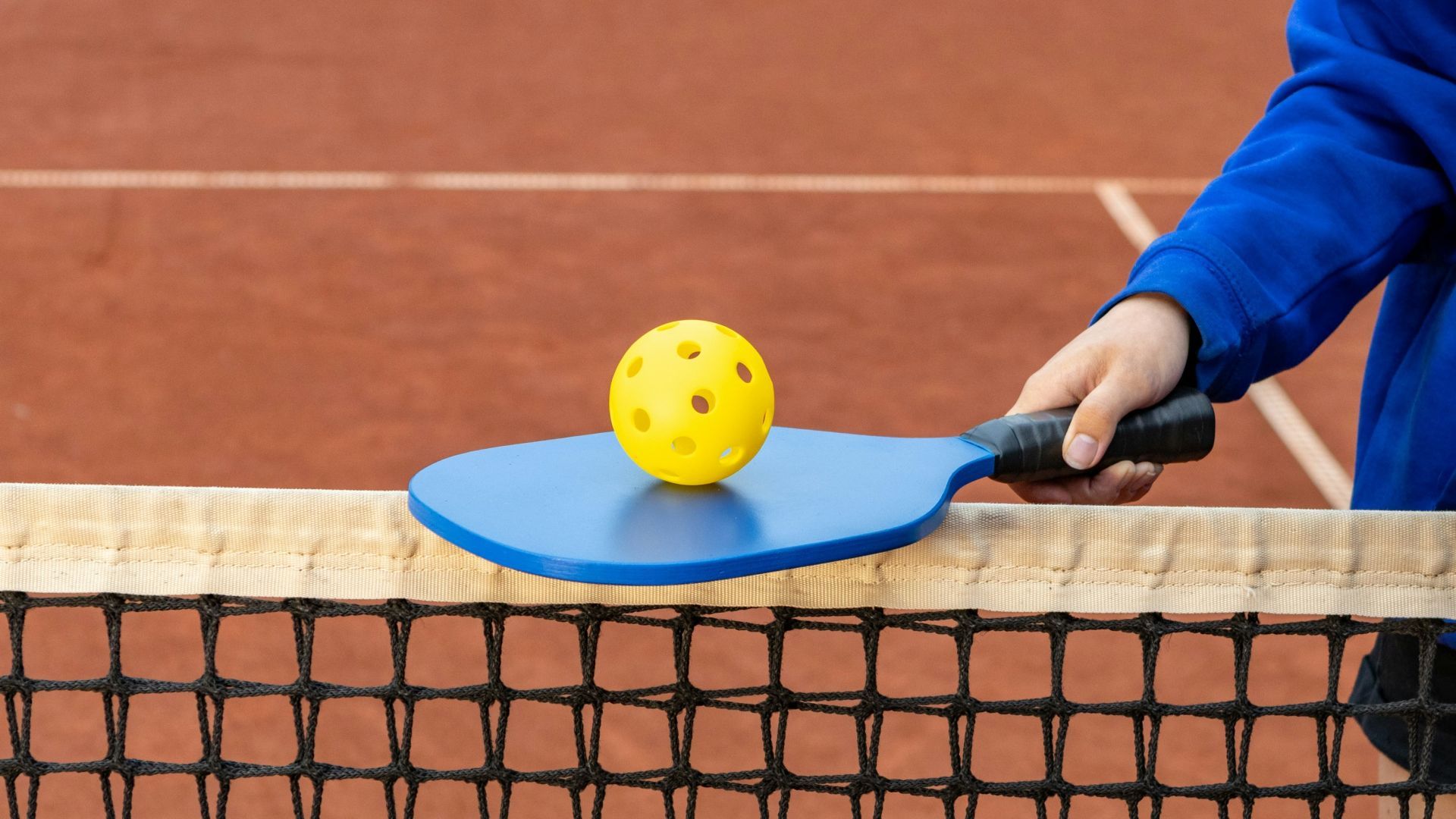 A person is holding a blue paddle with a yellow ball on it.