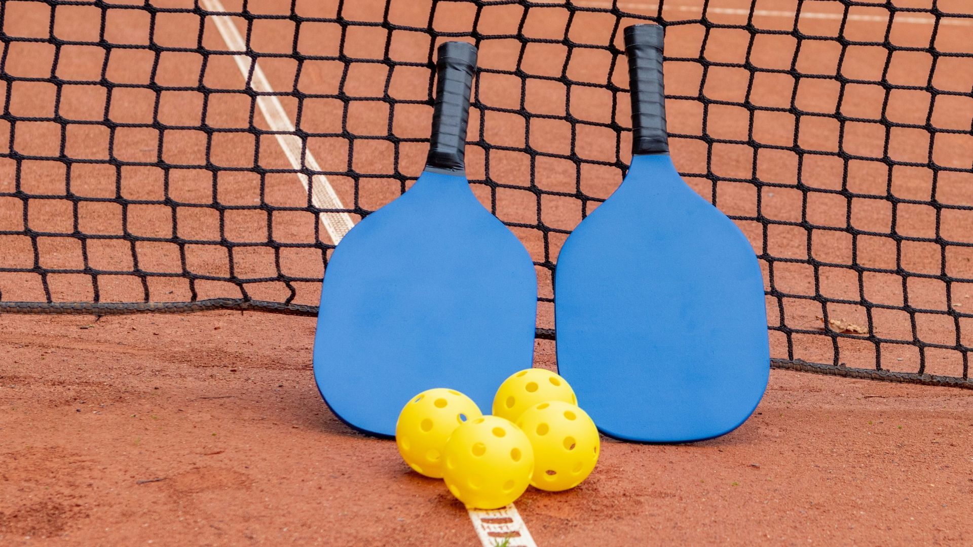 two blue rackets and yellow balls on a tennis court
