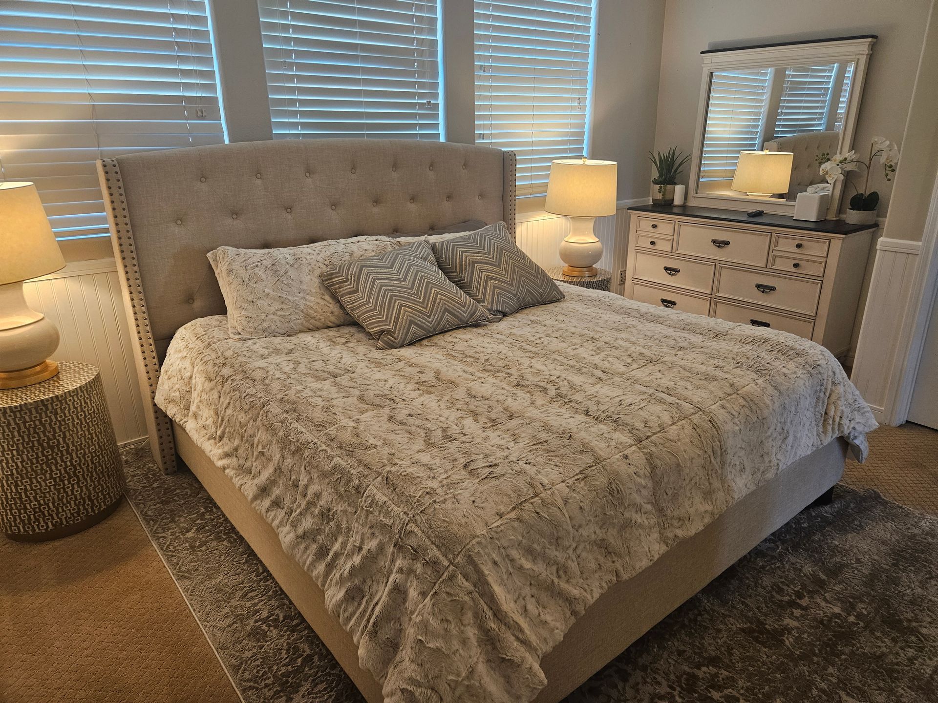 Cozy bedroom with a tufted bed, patterned bedding, bedside lamps, and a mirrored dresser.