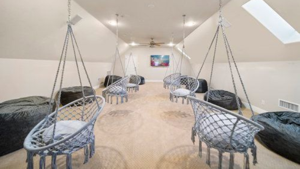 Loft lounge with hanging woven chairs, black cushions, and a skylight on a cream carpeted floor
