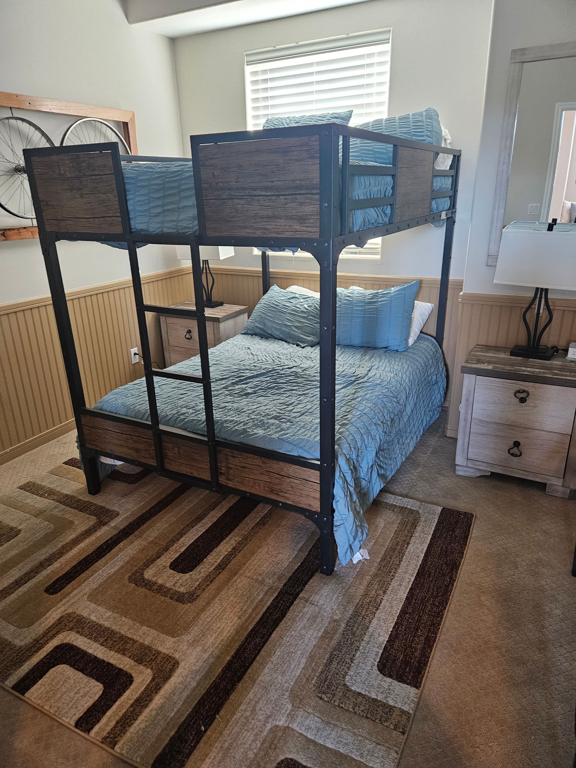 Lofted bunk bed in a bright bedroom with blue bedding and a striped rug
