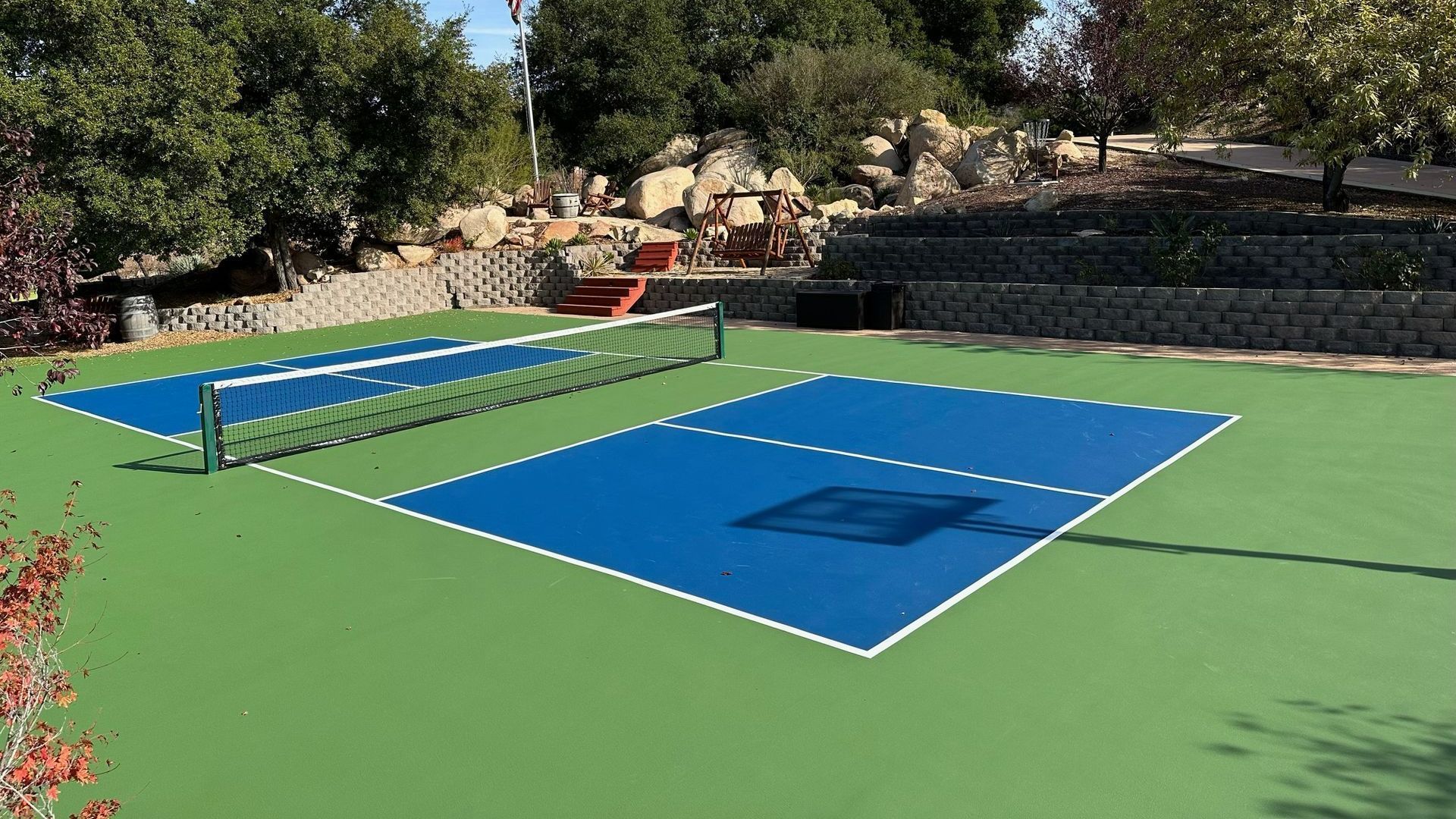 A blue and green tennis court with trees in the background