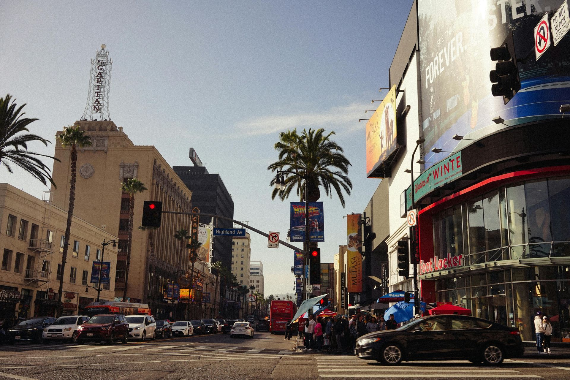 Busy city street with palm trees, cars, and tall buildings at an intersection.